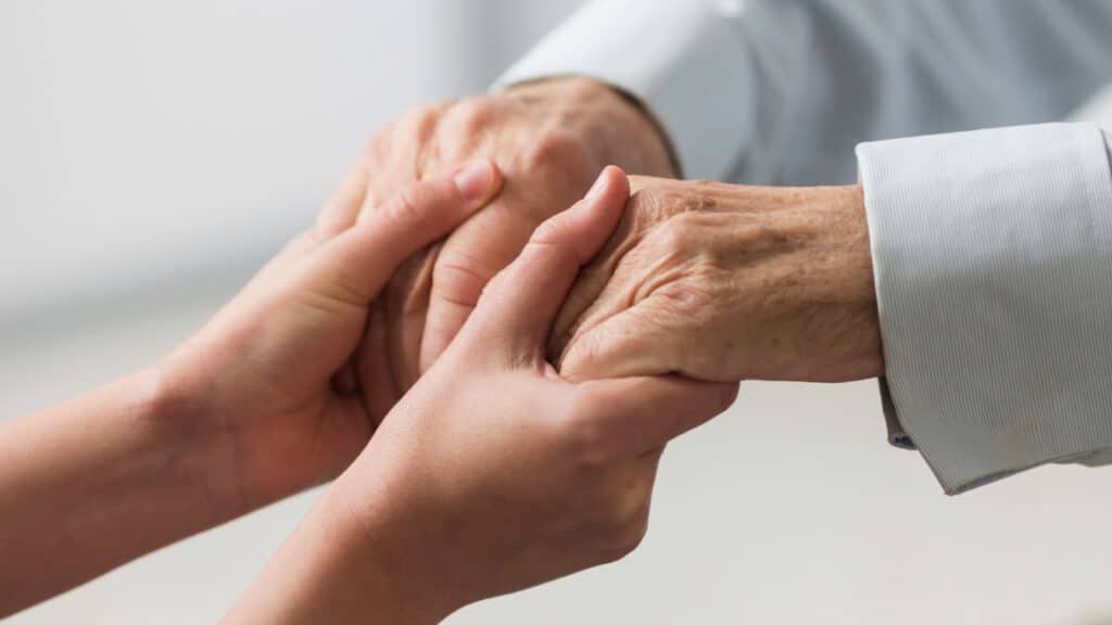 A caretaker reaching out to hold a patient's hands